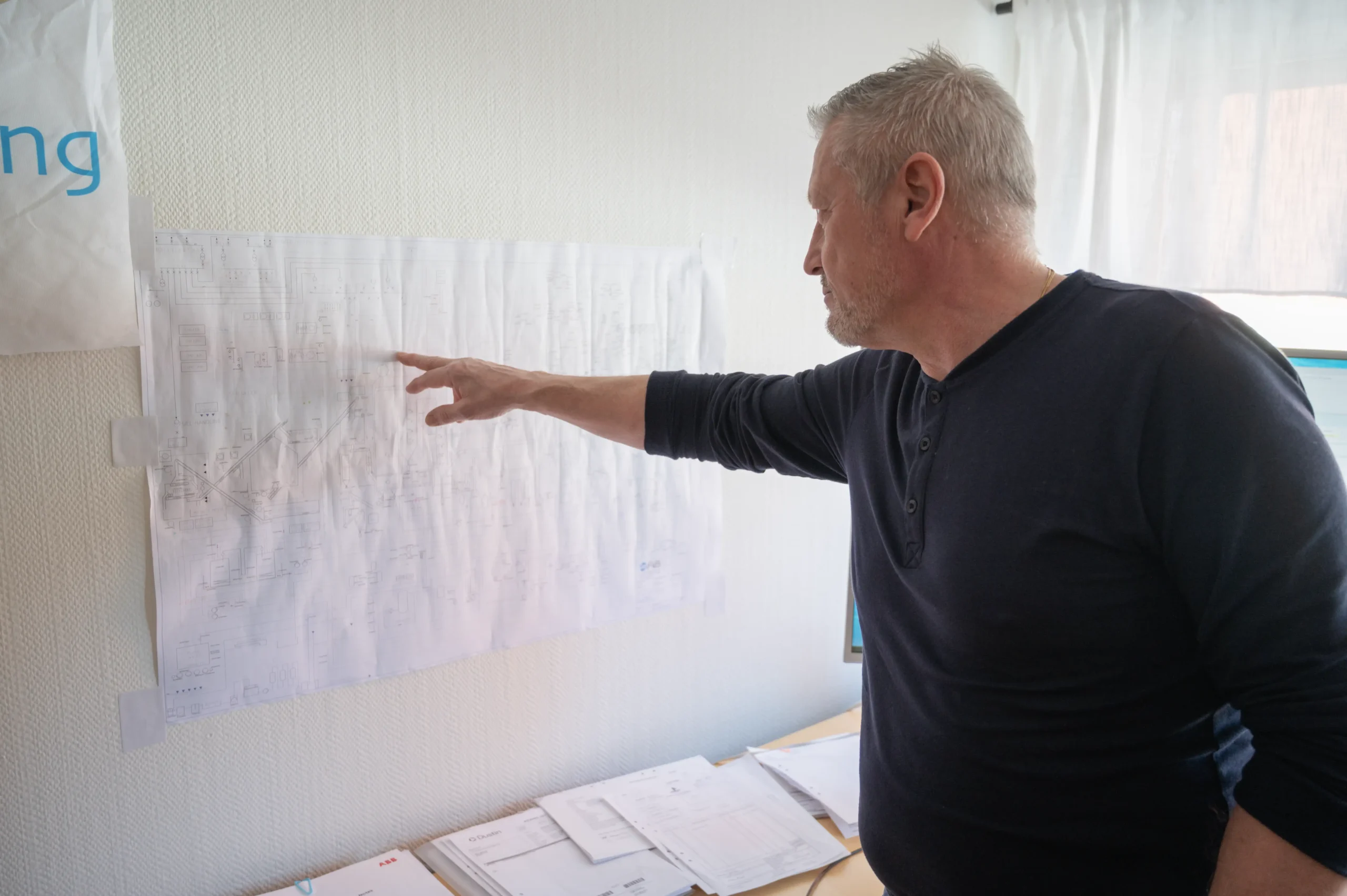 Ole Kaustinen pekar på ett papper med ritningar som tejpats upp på väggen.